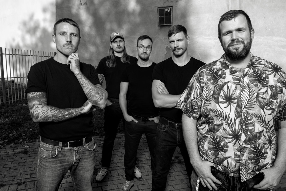 Schwarz/weiß-Bandfotografie von "Feine Sahne Fischfilet". Fünf männlich gelesene Personen stehen in einem V angeordnet vor der Kamera und blicken in diese.