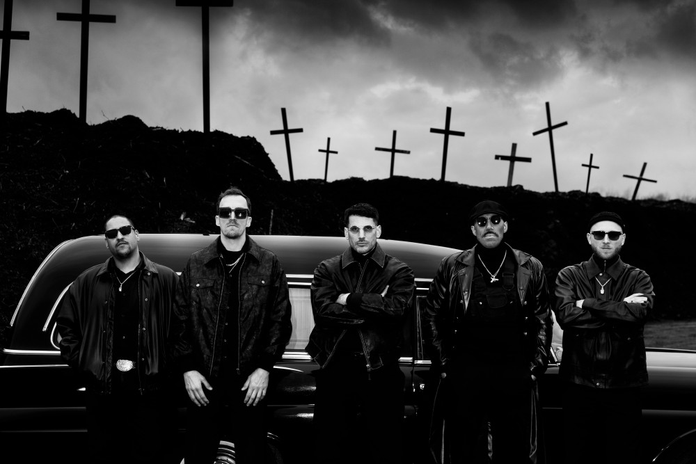 Auf dem Bild befinden sich 5 männlich gelesene Personen, welche vor einem Auto stehen. Im Hintergrund sind viele Kreuze.