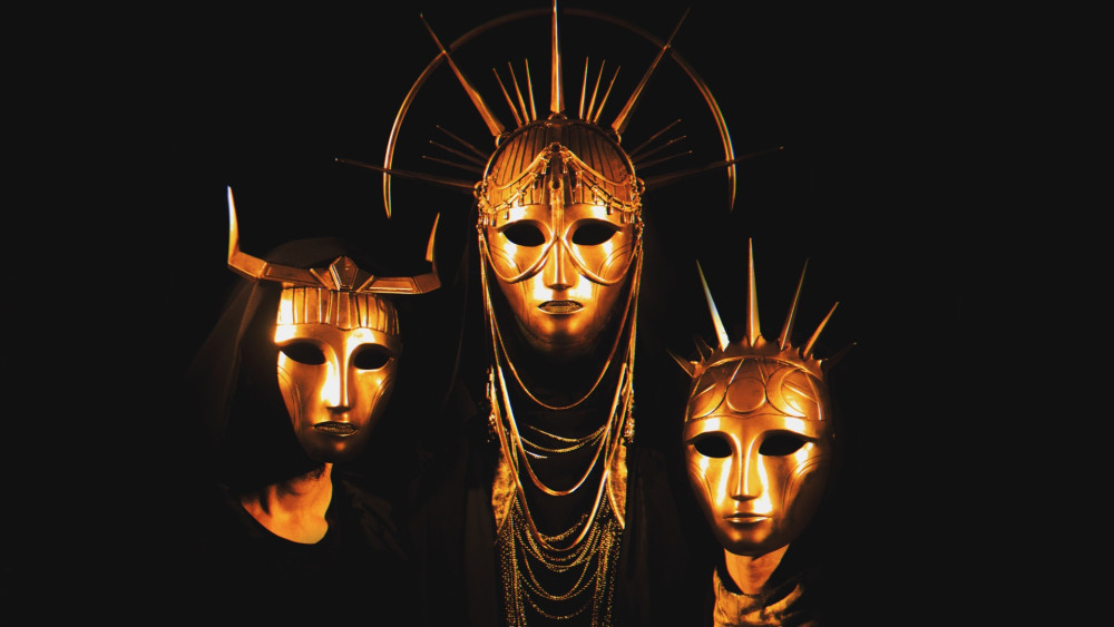 Auf dem Bild sind drei goldene Masken zu sehen. Die Augen sind komplett schwarz und die Masken zeigen keine Gesichtsausdrücke.